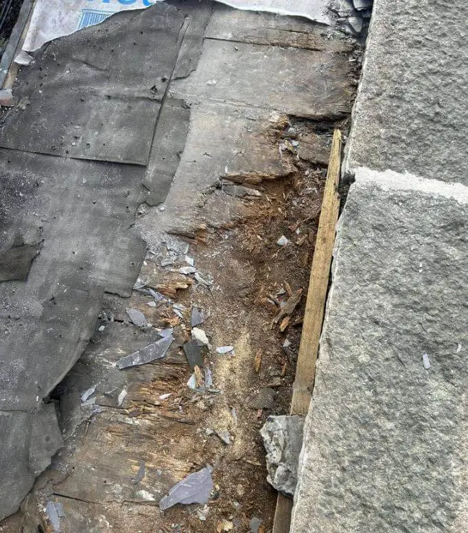 Damaged flat roof covering beside a parapet wall