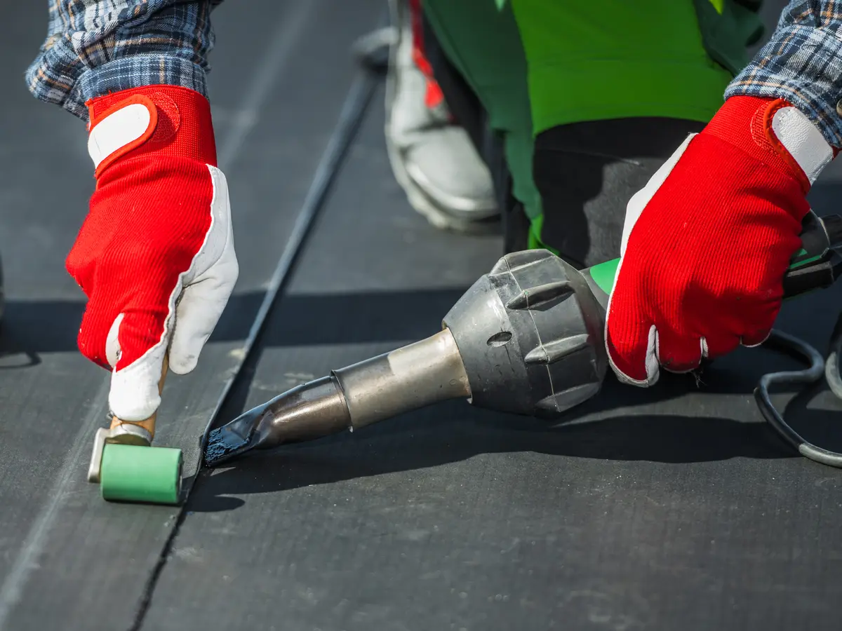 Roofer sealing a black rubber membrane seam with a roller