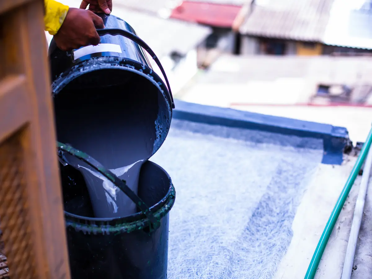 Roofer pouring resin onto fibreglass matting on a flat roof