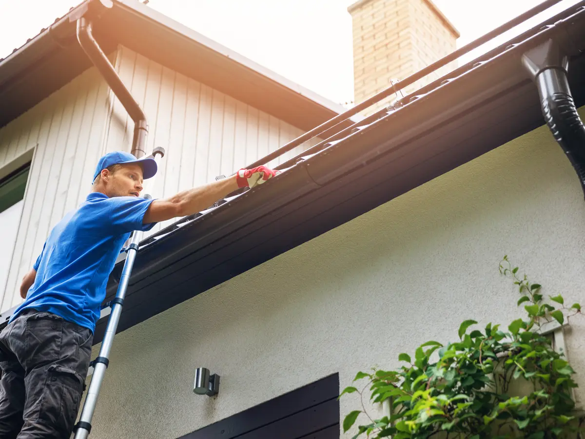 Man on a ladder clearing a blocked house gutter