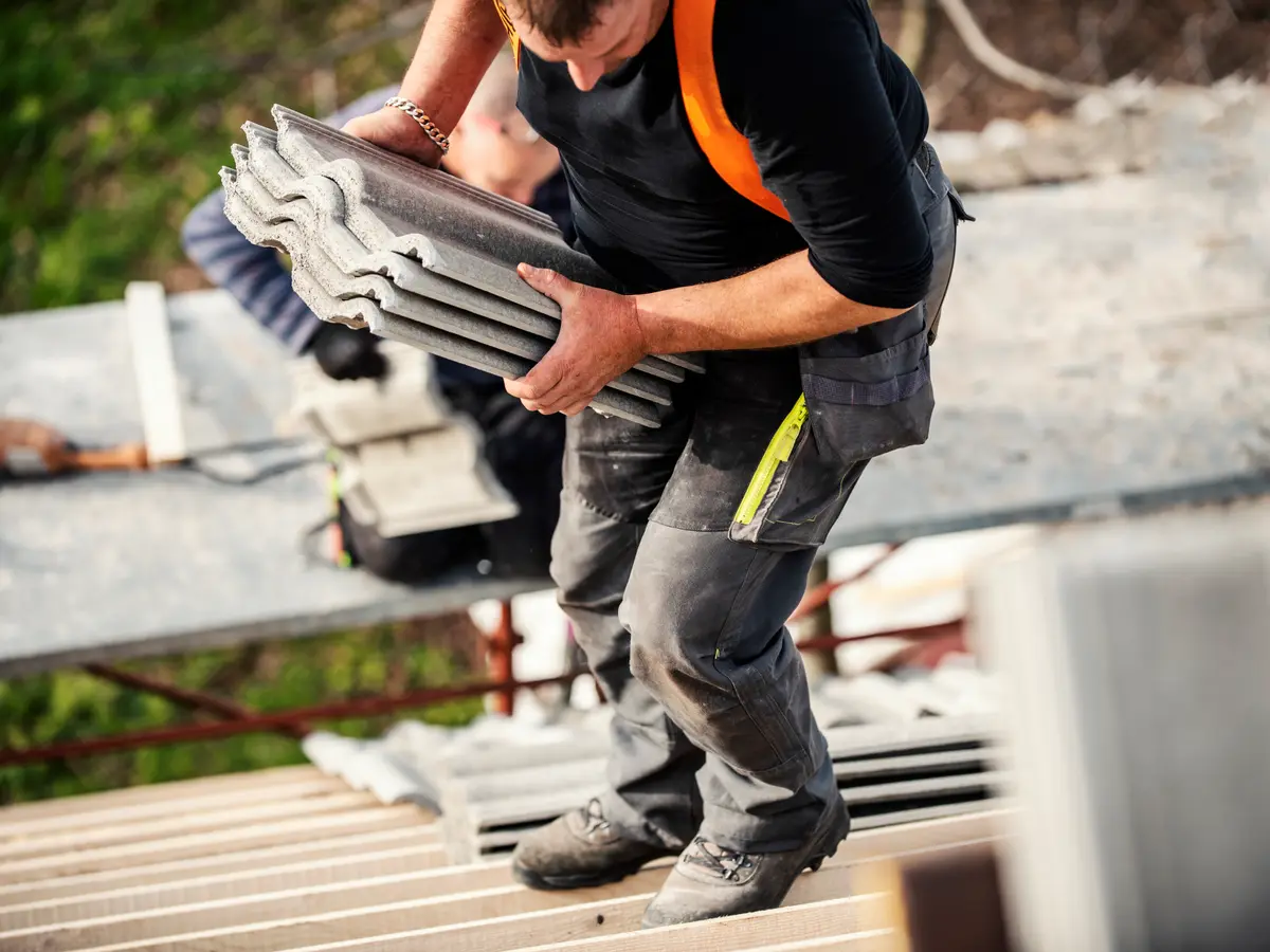 Roofer carrying new roof tiles across the battens