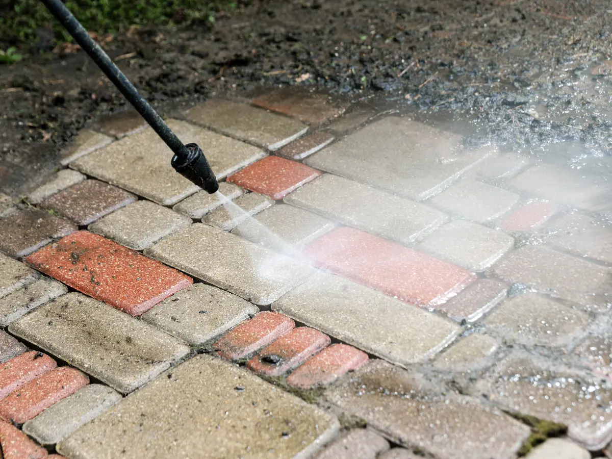 Pressure washer cleaning red and buff block paving