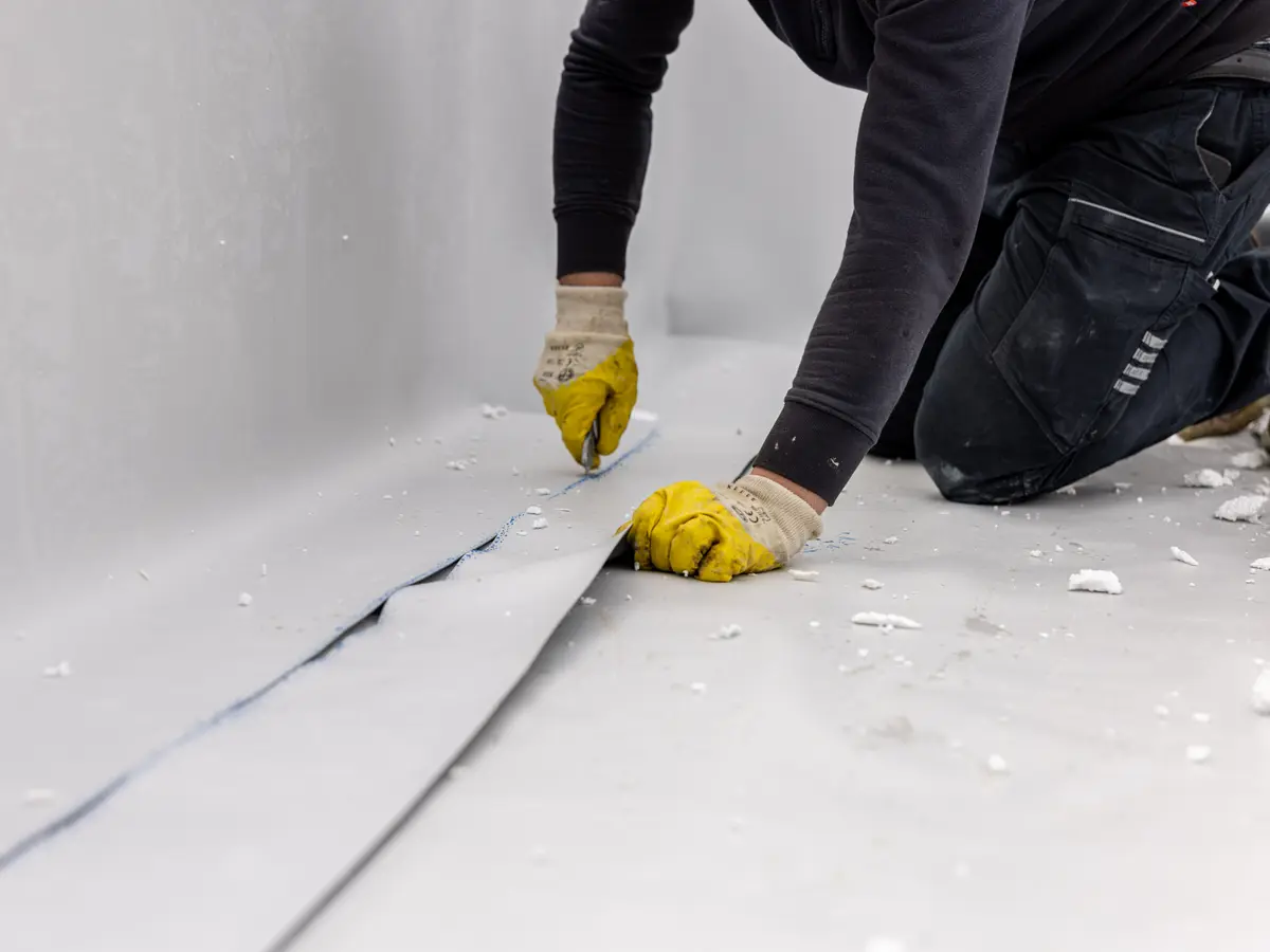 Roofer trimming a single ply membrane on a flat roof