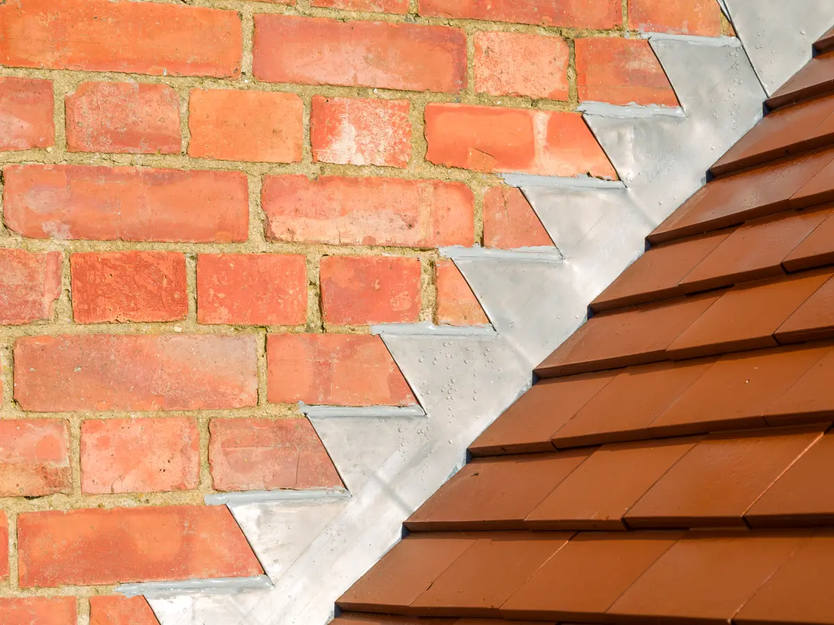 Lead step flashing between brickwork and clay plain tiles