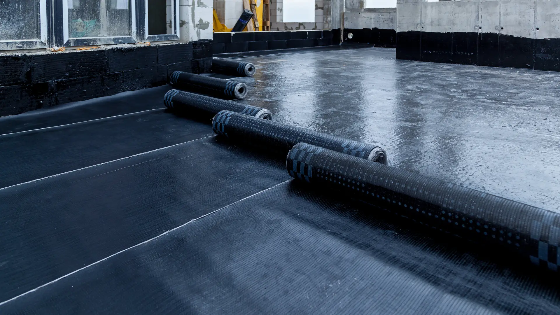 Rolls of black rubber membrane laid out across a new flat roof