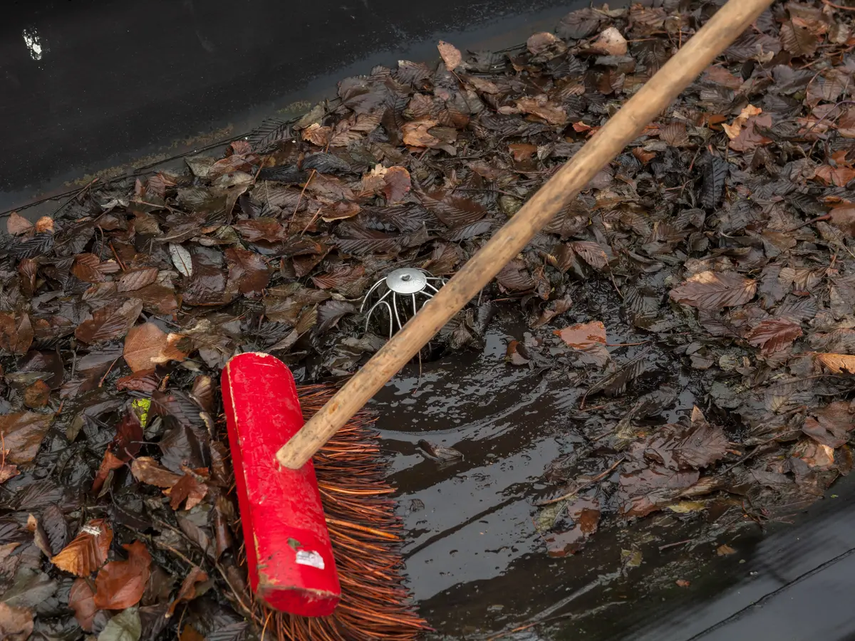 Broom sweeping fallen leaves out of a roof gutter