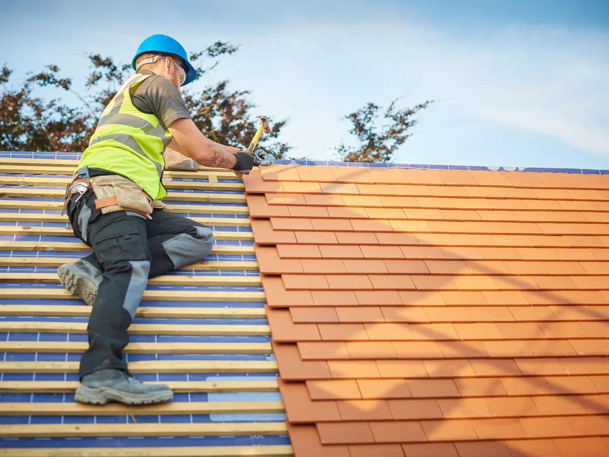 Roofer laying clay plain tiles over new battens